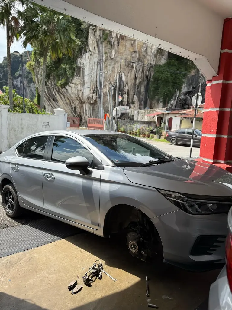 Silver sedan parked outside the bay with a front wheel removed, tools on the ground and a limestone hill behind