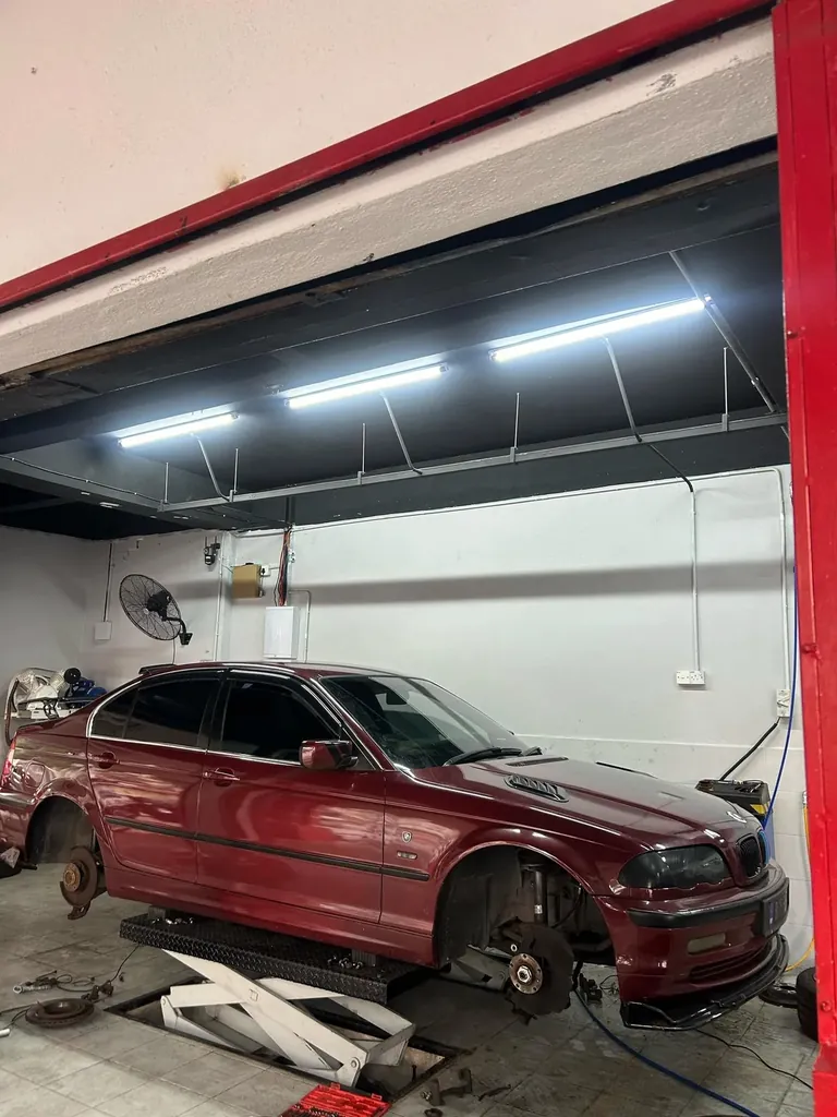 Dark red BMW saloon with its wheels removed inside the workshop bay under fluorescent lights