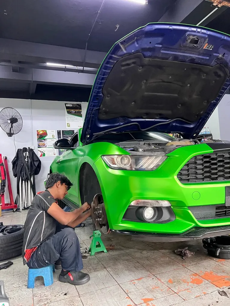 Green wrapped sports coupe with its bonnet up while a technician sits at the front wheel working on the brake