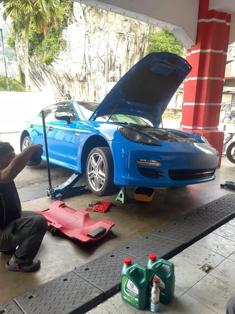 Blue sedan jacked at the front with its bonnet raised and two bottles of engine oil on the floor