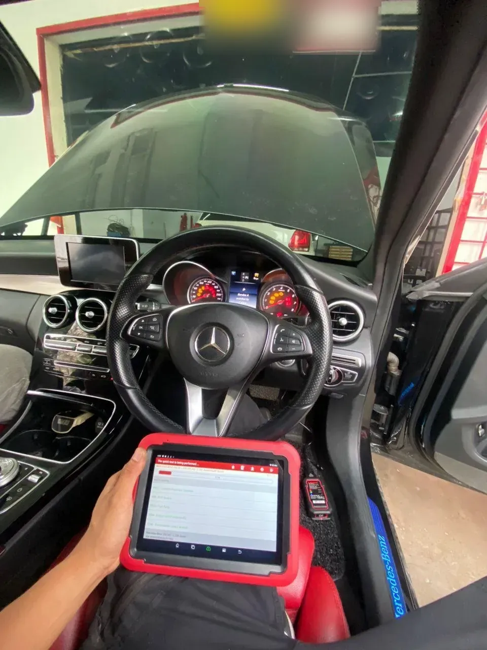 Otoka Garage technician holding a diagnostic scan tablet in the driver's seat of a Mercedes-Benz