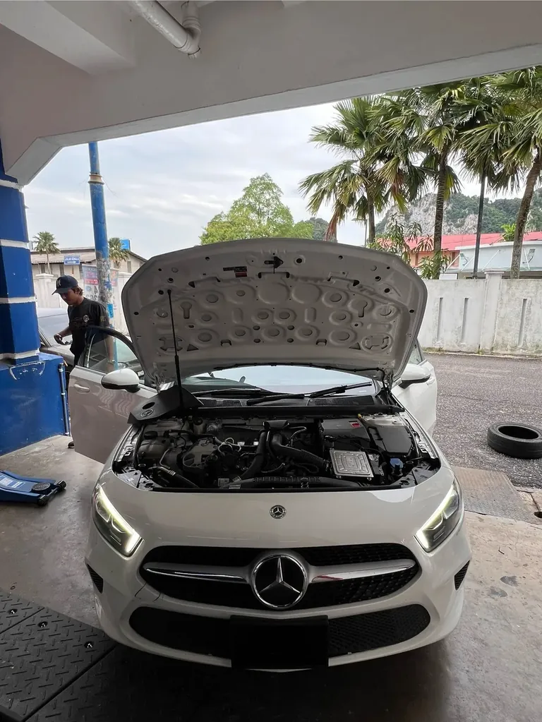 White Mercedes-Benz hatchback with its bonnet open and a technician at the driver's door