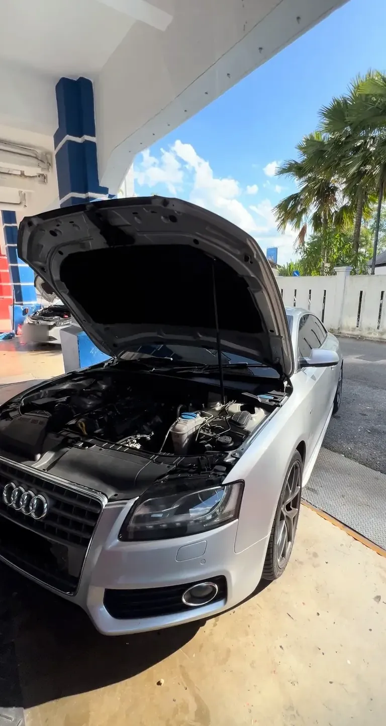 Silver Audi with its bonnet raised under the canopy against a blue sky