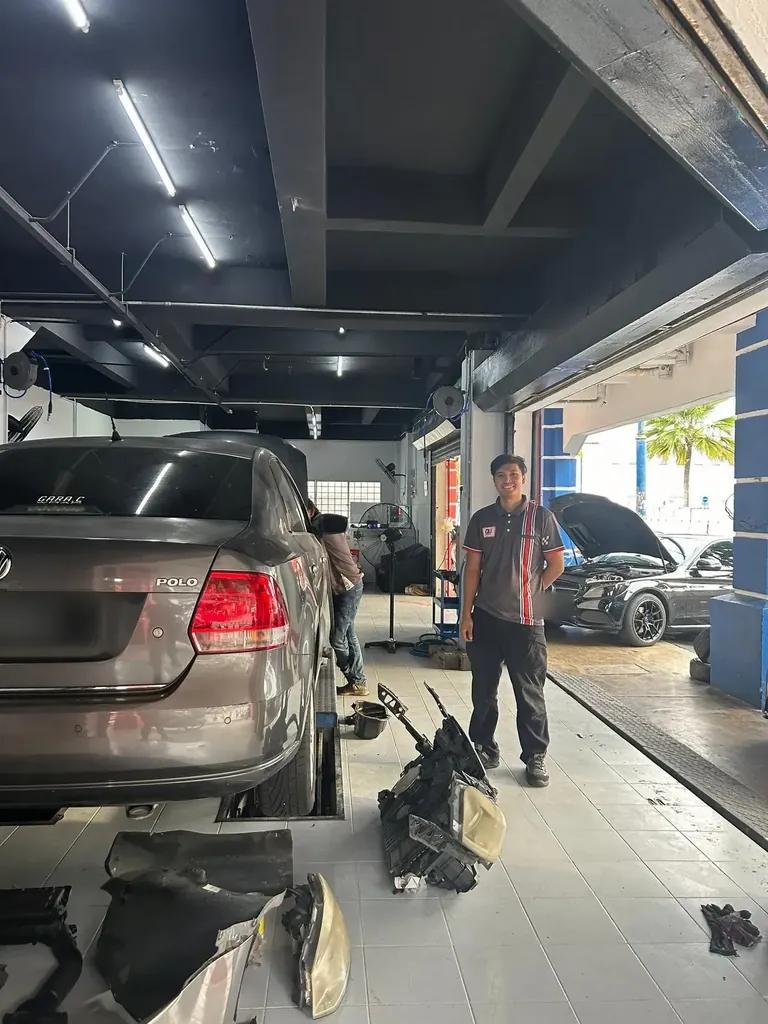 Volkswagen Polo over a service bay with a technician standing beside it and parts laid on the floor
