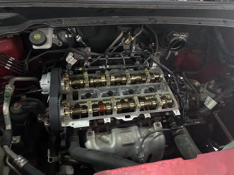 Engine bay with the cam cover removed, showing twin camshafts and the timing belt
